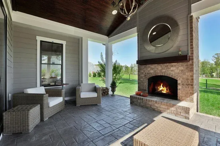 Covered patio with brick fireplace, wicker seating, and views of a green yard