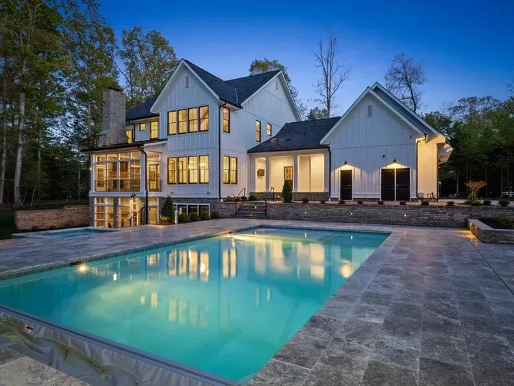 Modern house with a lit patio and turquoise swimming pool at dusk
