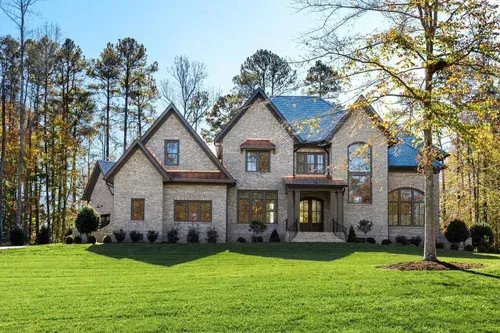 Large stone house with a manicured green lawn and trees under a clear sky