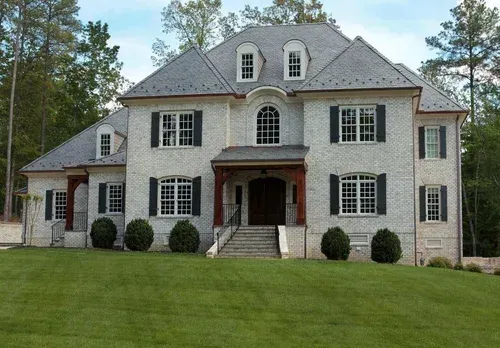 Large gray two-story house with black shutters and a manicured lawn surrounded by trees