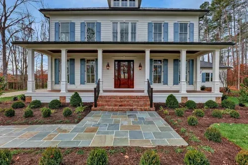 Front view of a white colonial-style house with blue shutters, a red door, and a brick porch with stone walkway