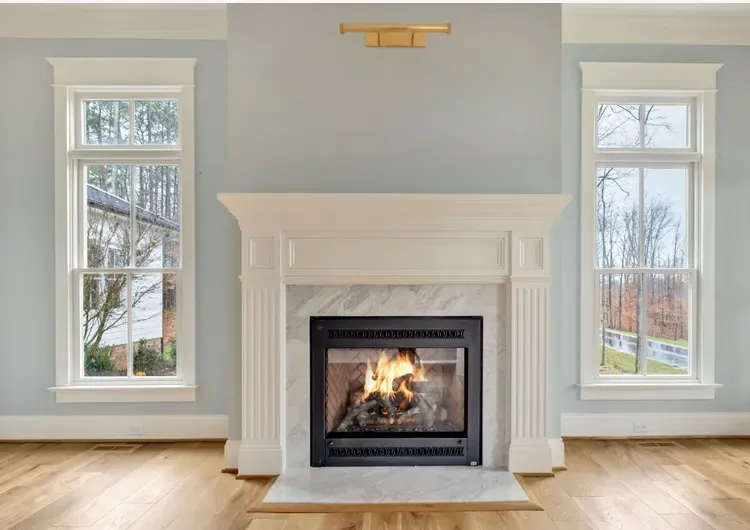 Bright living room with a white fireplace centered between two tall windows and light hardwood floors