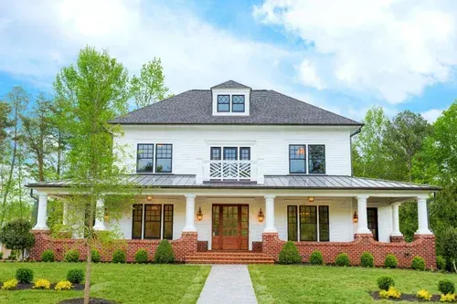 Large white two-story house with a front porch, brick base, and a green lawn.
