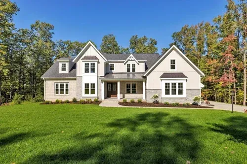 Large white suburban house with a front porch, dormer windows, and a wide green lawn under a blue sky