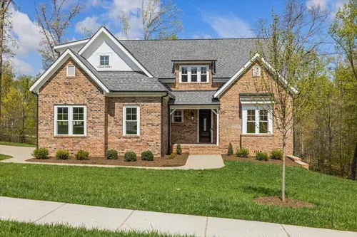 Brick suburban house with gray roof, front porch, and green lawn under a blue sky