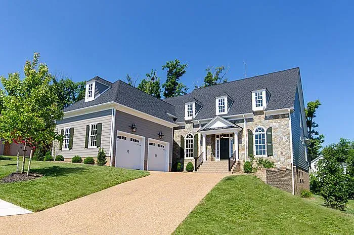 Large gray suburban house with white trim, garage, and a sloped driveway under a clear blue sky