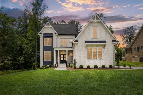 Modern two-story suburban house with white brick, dark trim, and a green lawn at sunset