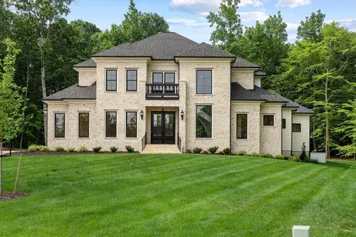 Large beige two-story house with a manicured green lawn and trees in the background