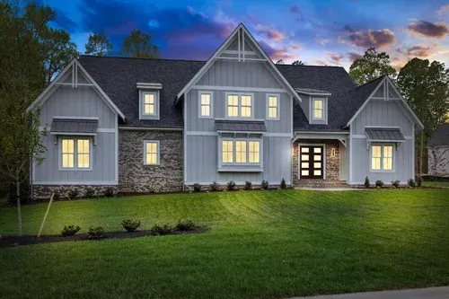 Large gray house with lit windows and a manicured lawn at dusk
