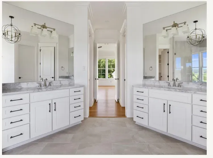 Bright double vanity bathroom with white cabinets, marble counters, and arched doorway to a sunlit room