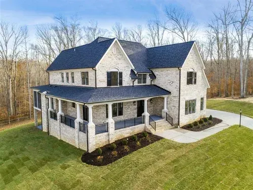 Stone two-story suburban house with dark roof, wraparound porch, and large green lawn
