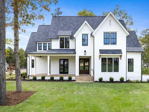 Large white two-story house with dark gray roof, black trim, and a front porch, surrounded by a green lawn.