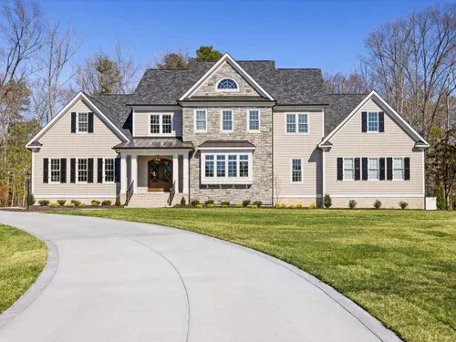 Large beige suburban house with a curved driveway and manicured lawn under a clear blue sky
