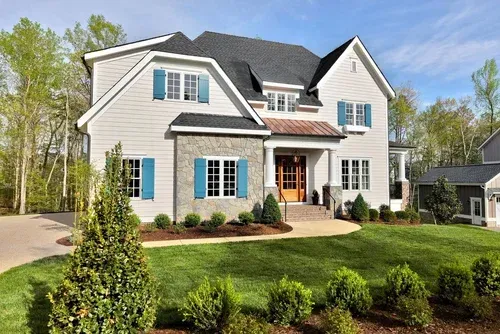 Modern two-story white suburban house with blue shutters, black roof, and landscaped front yard