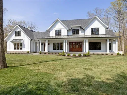Large white farmhouse-style house with a covered porch, gabled roof, and wide lawn