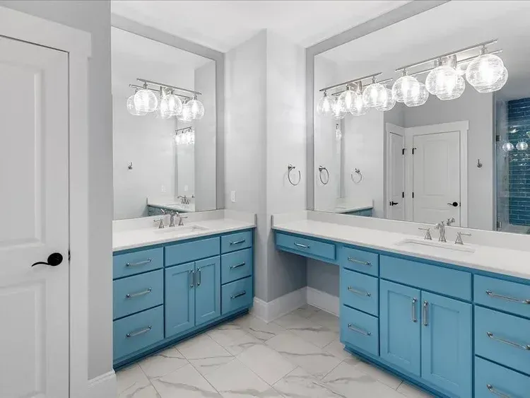 Bright bathroom vanity with blue cabinets, white countertops, large mirror, and globe light fixtures