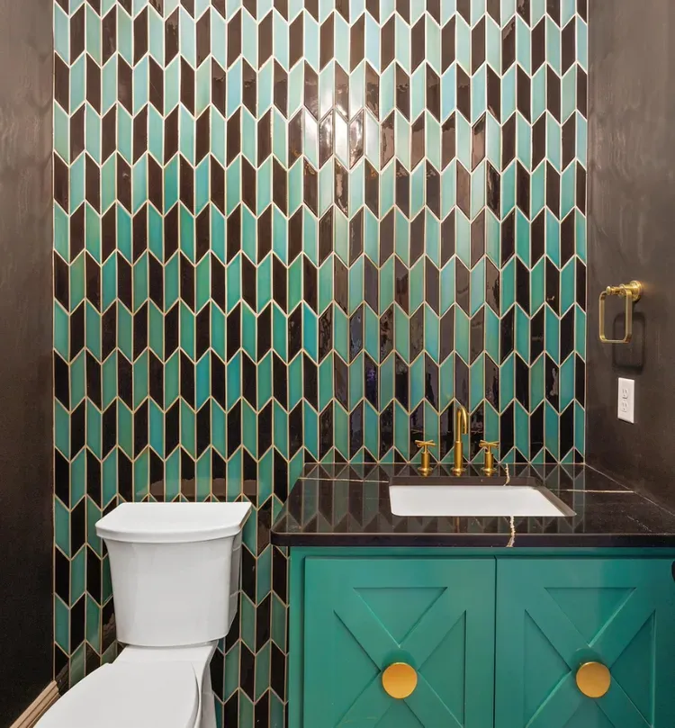 Stylish bathroom with teal geometric tile, white toilet, and green vanity with gold accents.