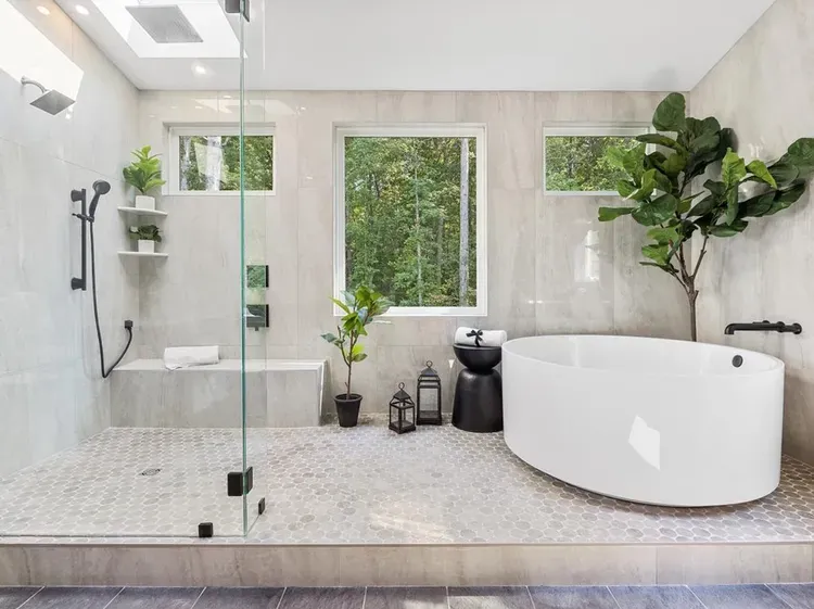 Modern spa-like bathroom with glass shower, freestanding tub, and large windows overlooking greenery