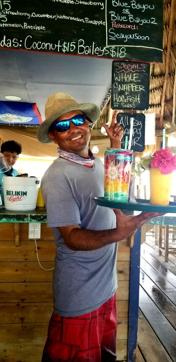 A man wearing a straw hat and sunglasses is holding a tray of drinks.