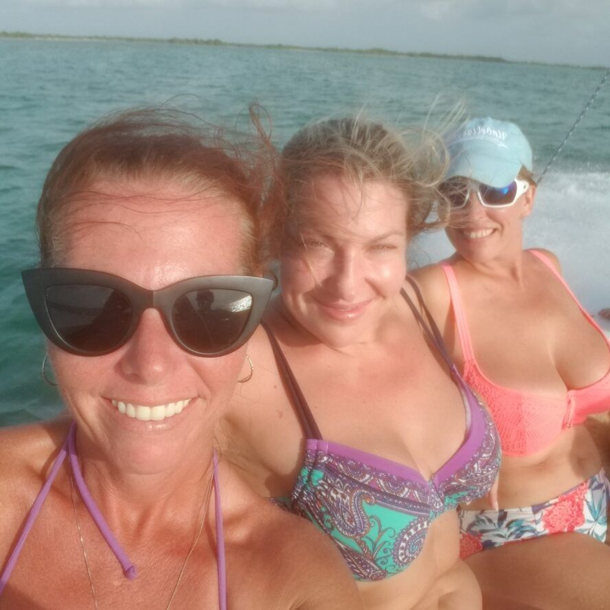 Three women in bikinis are sitting on a boat in the ocean.