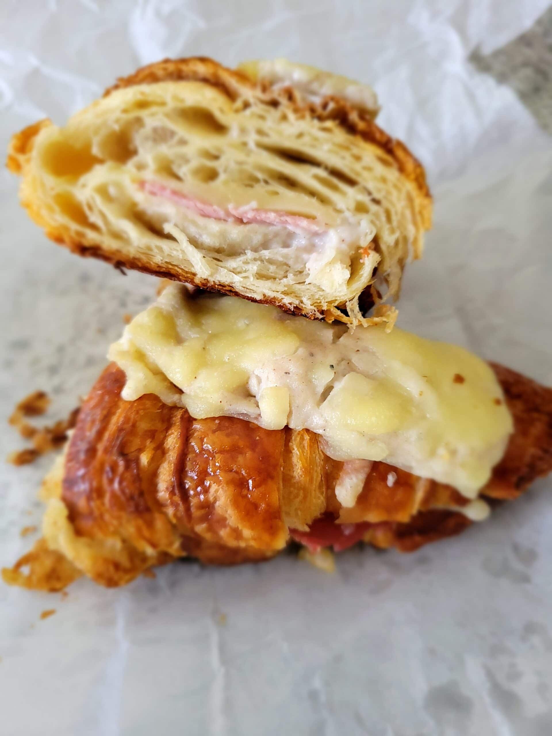 A close up of a croissant sandwich cut in half on a piece of paper.