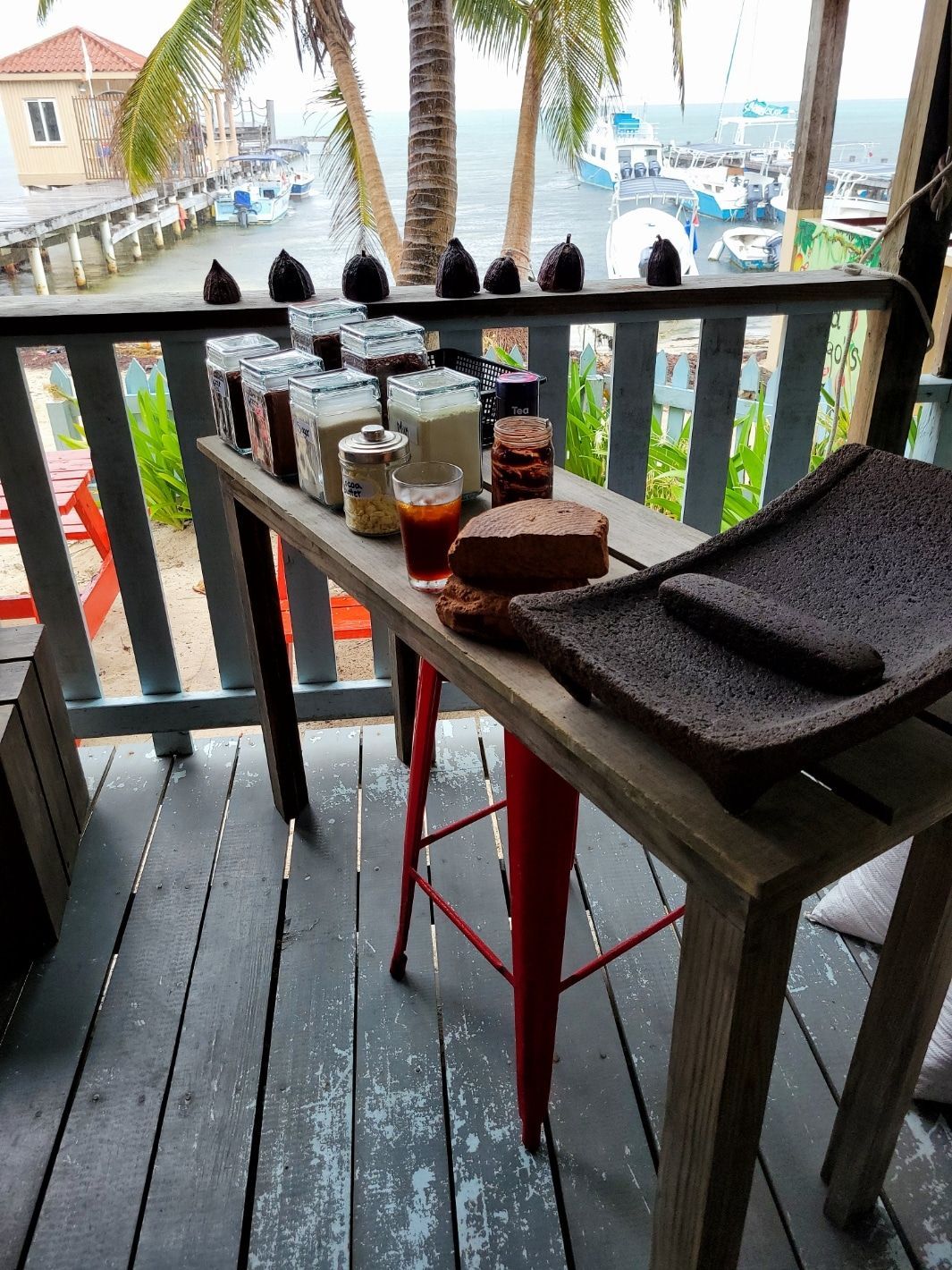 A wooden table with a red stool on a balcony overlooking the ocean.