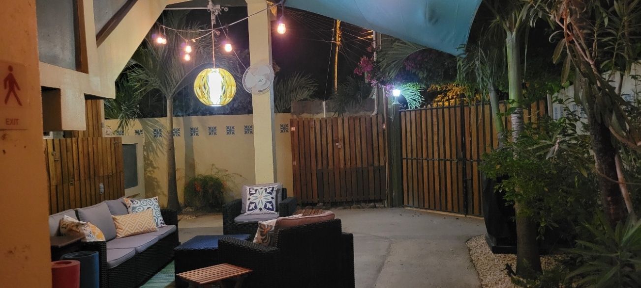 A patio with a couch , chairs , and a bamboo fence at night.
