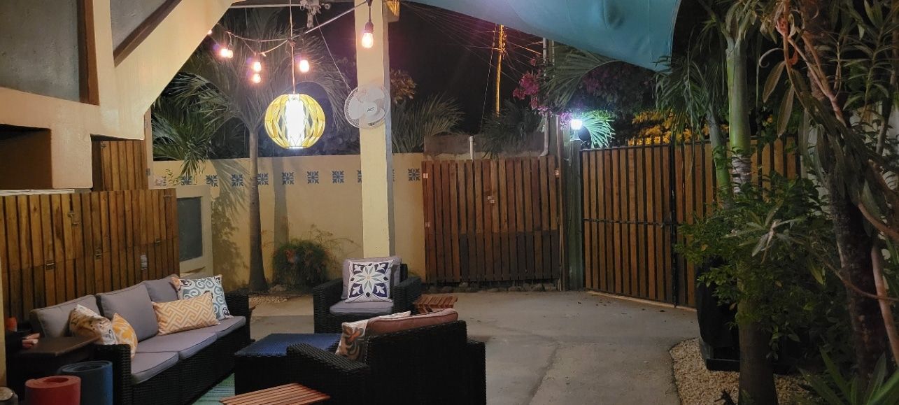 A patio with a couch , chairs , and a wooden fence at night.
