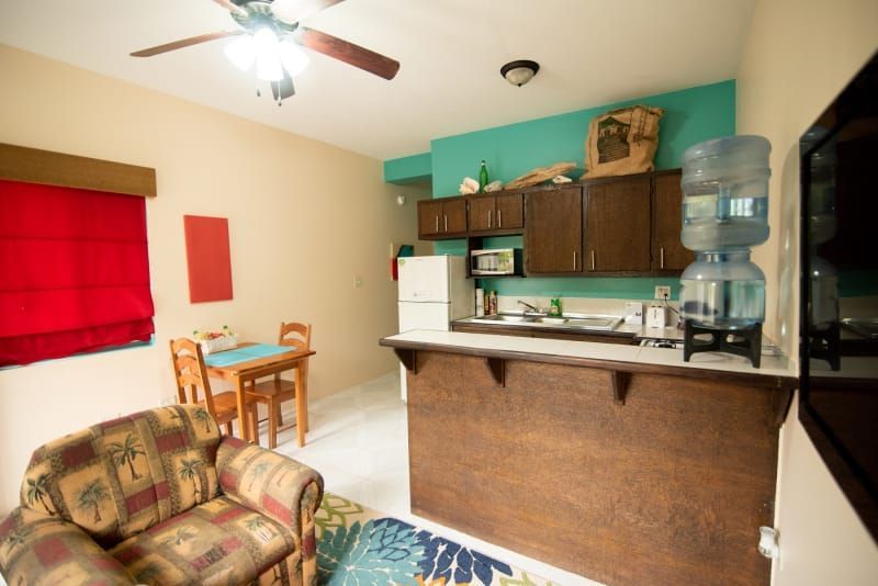 A living room with a table and chairs and a kitchen with a refrigerator.