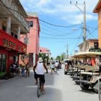 A man is riding a bike down a street next to a row of golf carts.