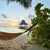 There is a hammock on the beach with a gazebo in the background.