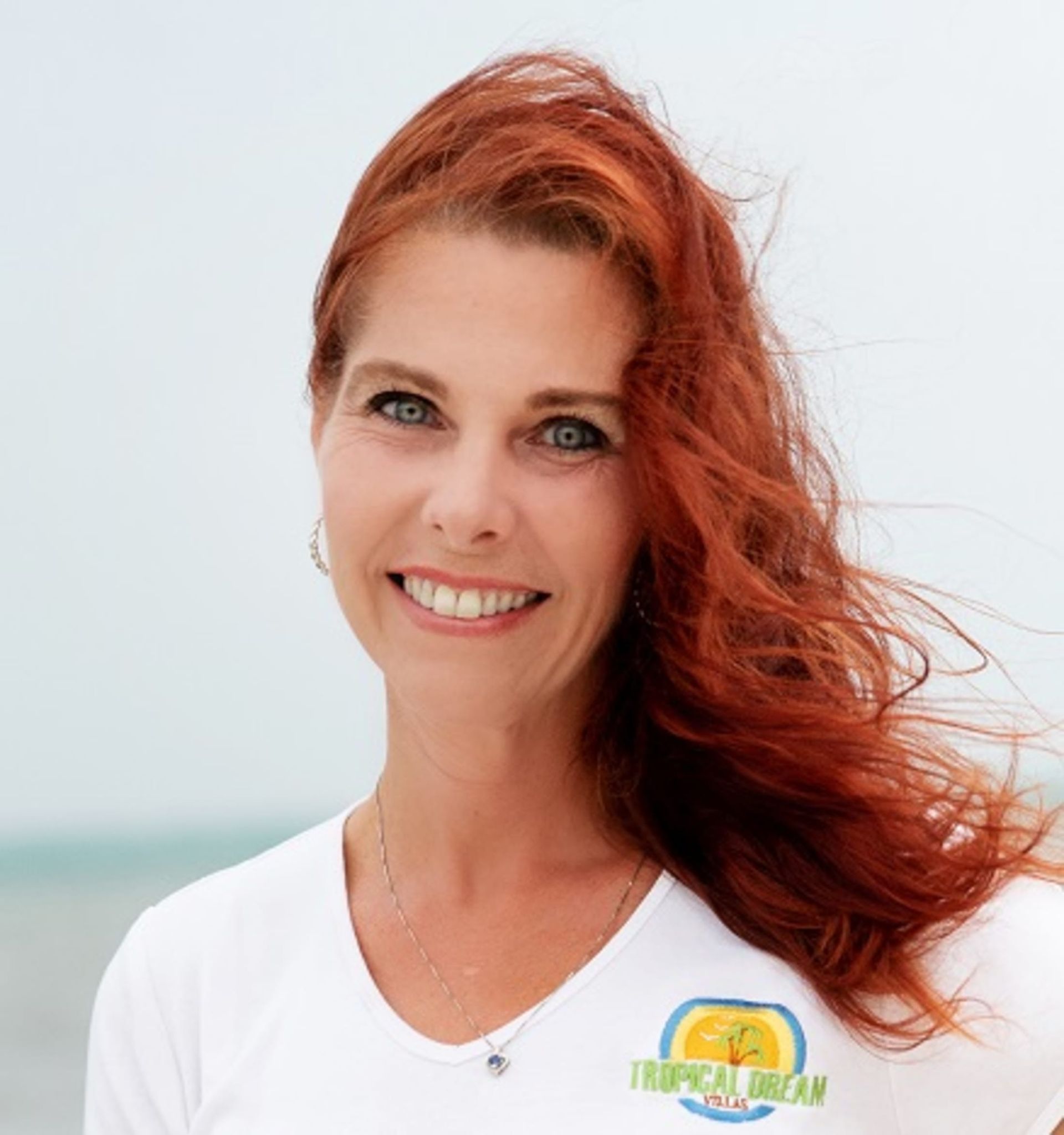 A woman with red hair is wearing a white shirt that says tropical dream