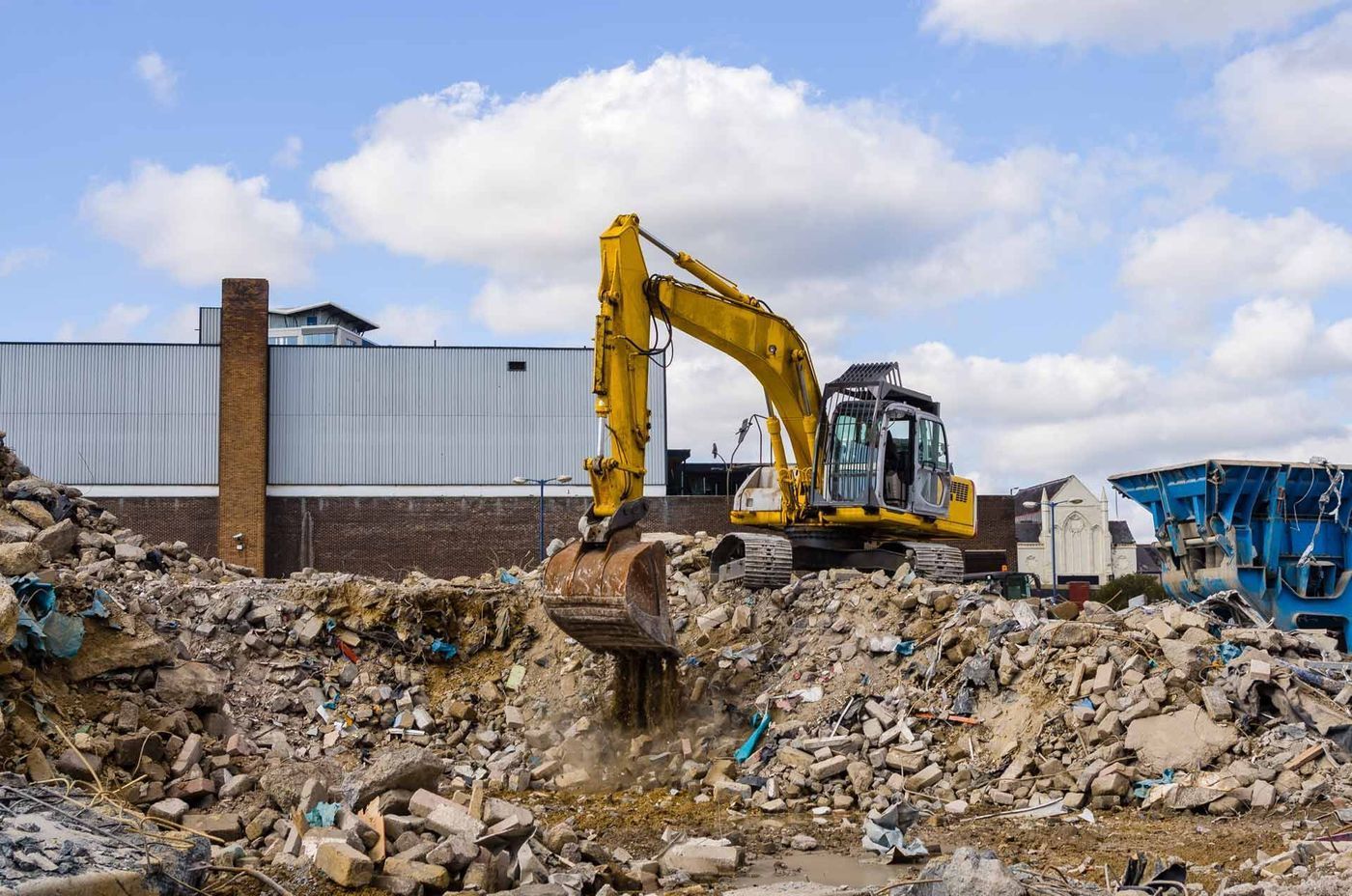 A yellow excavator is working on a pile of rubble.