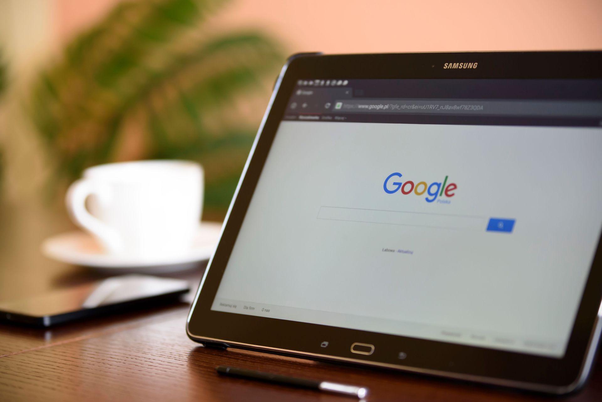 Tablet on a desk showing the Google homepage, with a coffee cup and notebook in the background.