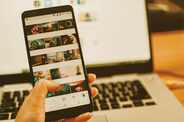 Hand holding phone showing a photo gallery in front of a laptop for social media content managed by Wilsona Marketing
