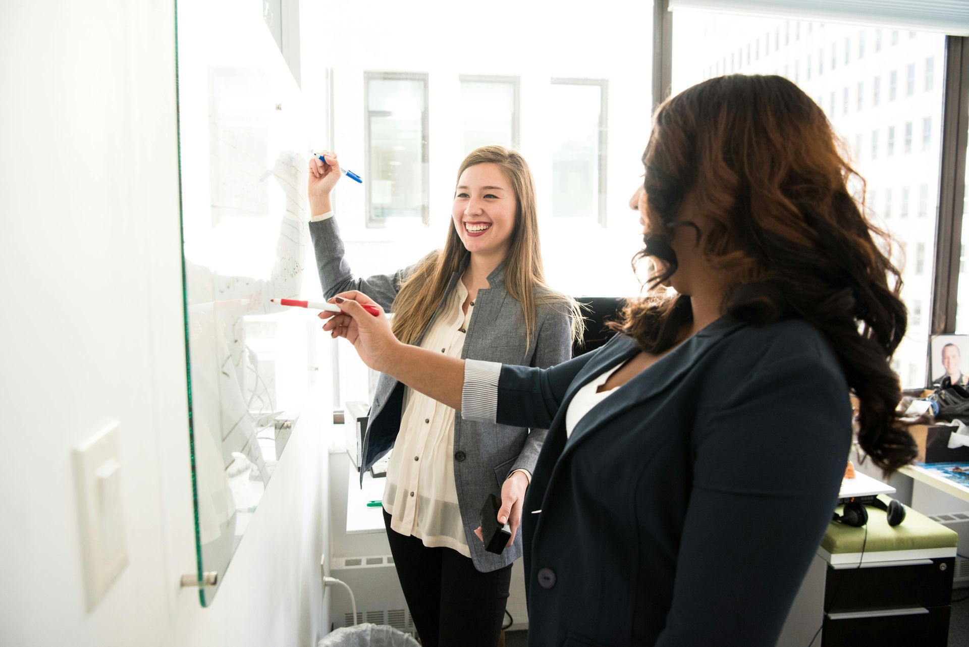Two colleagues writing on a whiteboard in a bright office meeting space at Wilsona Marketing