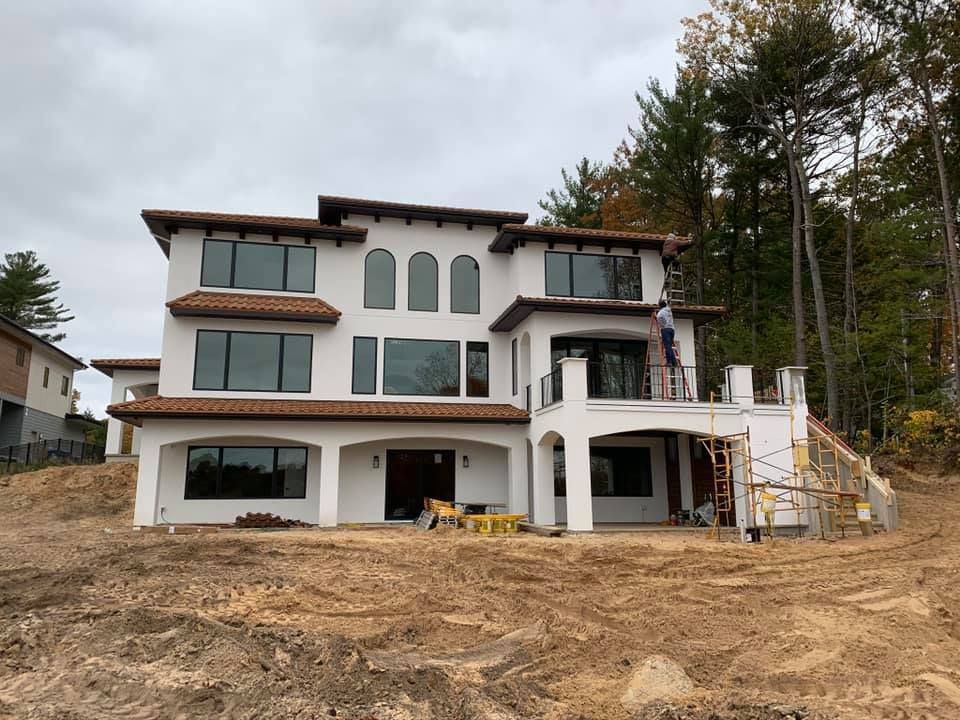 A large white house is sitting on top of a dirt hill surrounded by trees.