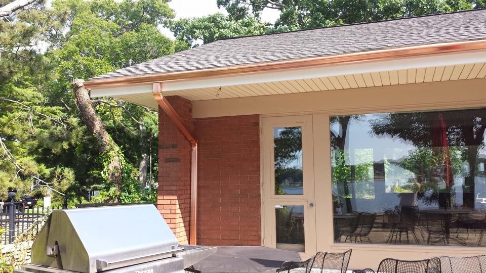 Building exterior with copper gutters, red brick, and large windows, likely overlooking water.