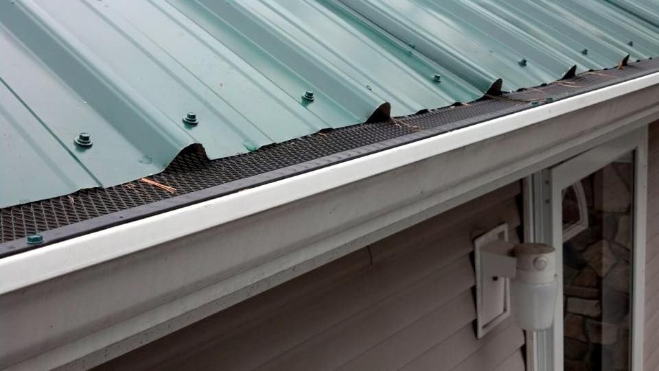 A green metal roof with a white gutter on the side of a house.