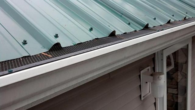 A green metal roof with a white gutter on the side of a house.