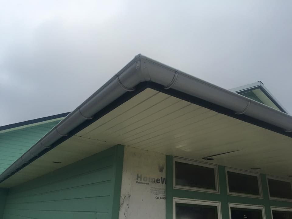 A green house with a white gutter on the roof