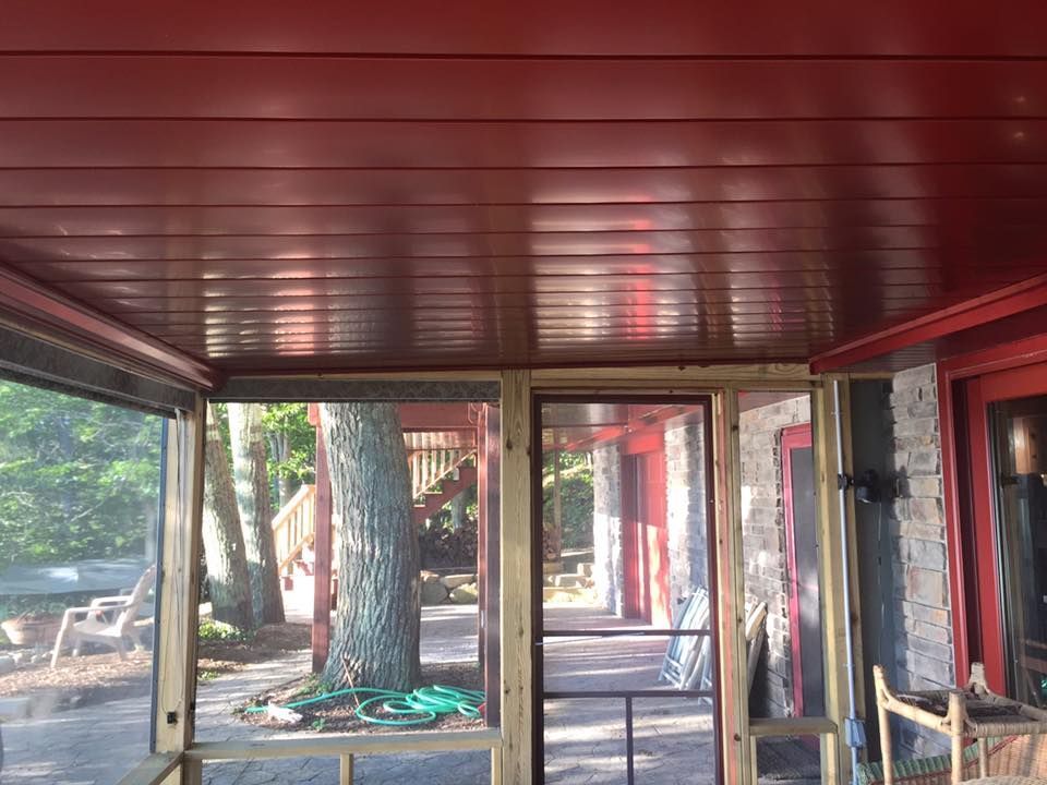A screened in porch with a red ceiling and a tree in the background.