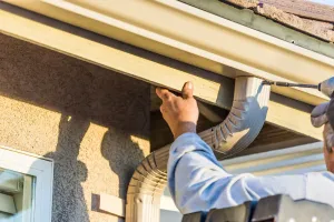 A man is installing a gutter on the side of a house.