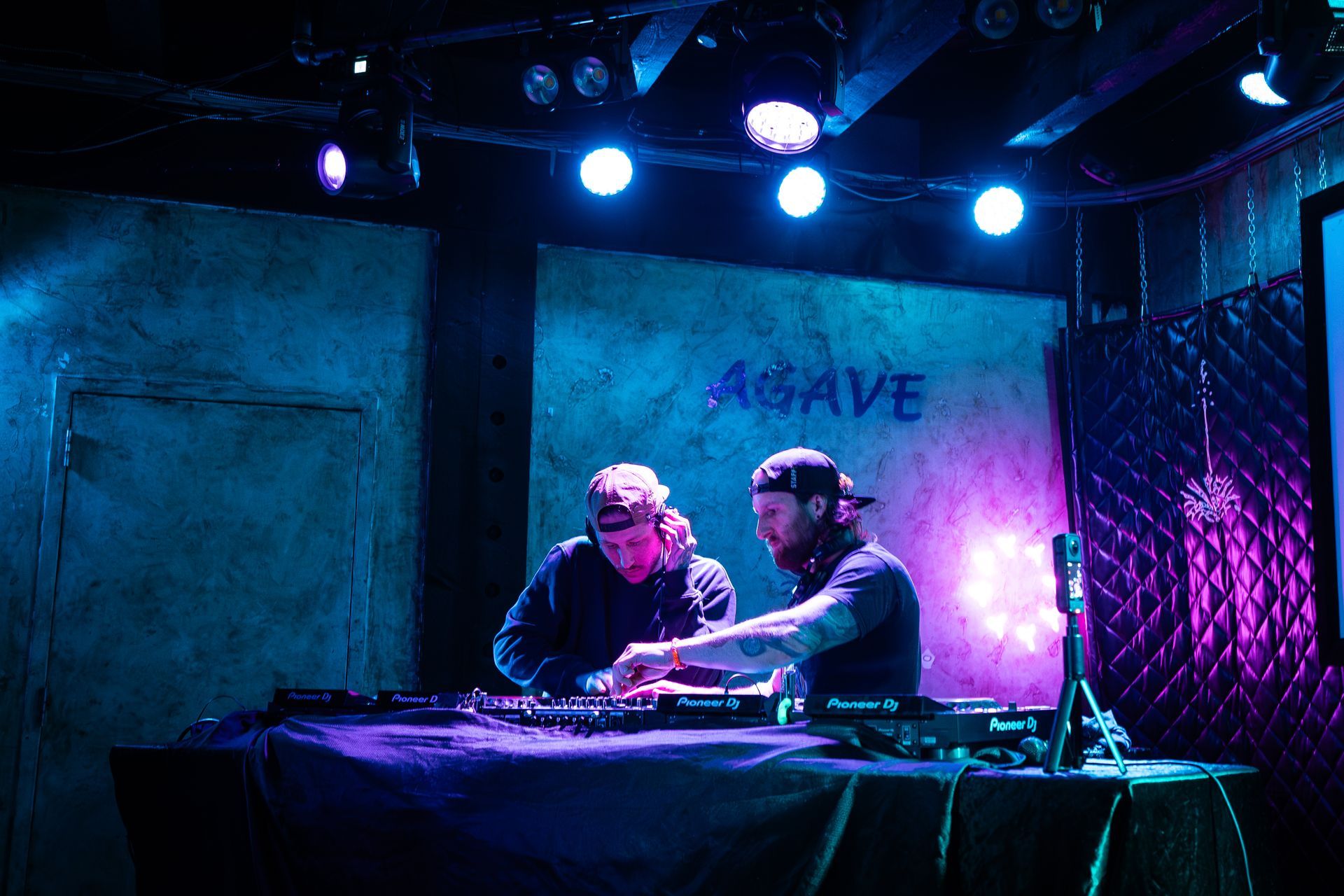 Two people operating DJ equipment at a venue called 