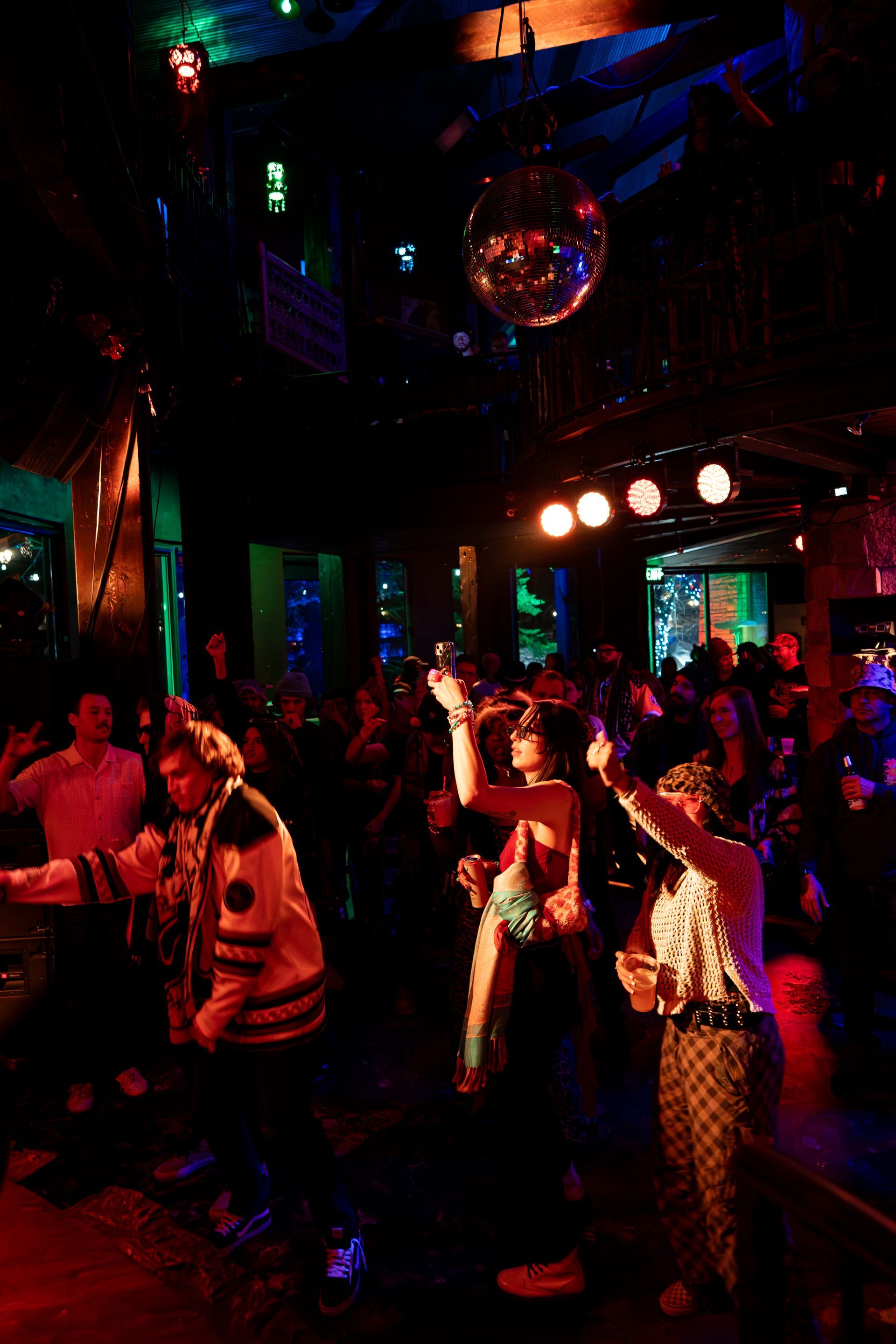 People dancing in a dimly lit club under a disco ball, arms raised.