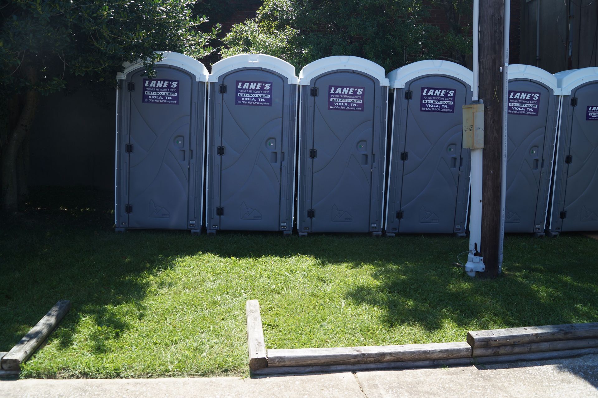 a brown and yellow portable toilet is sitting on a sidewalk next to a blue dumpster .