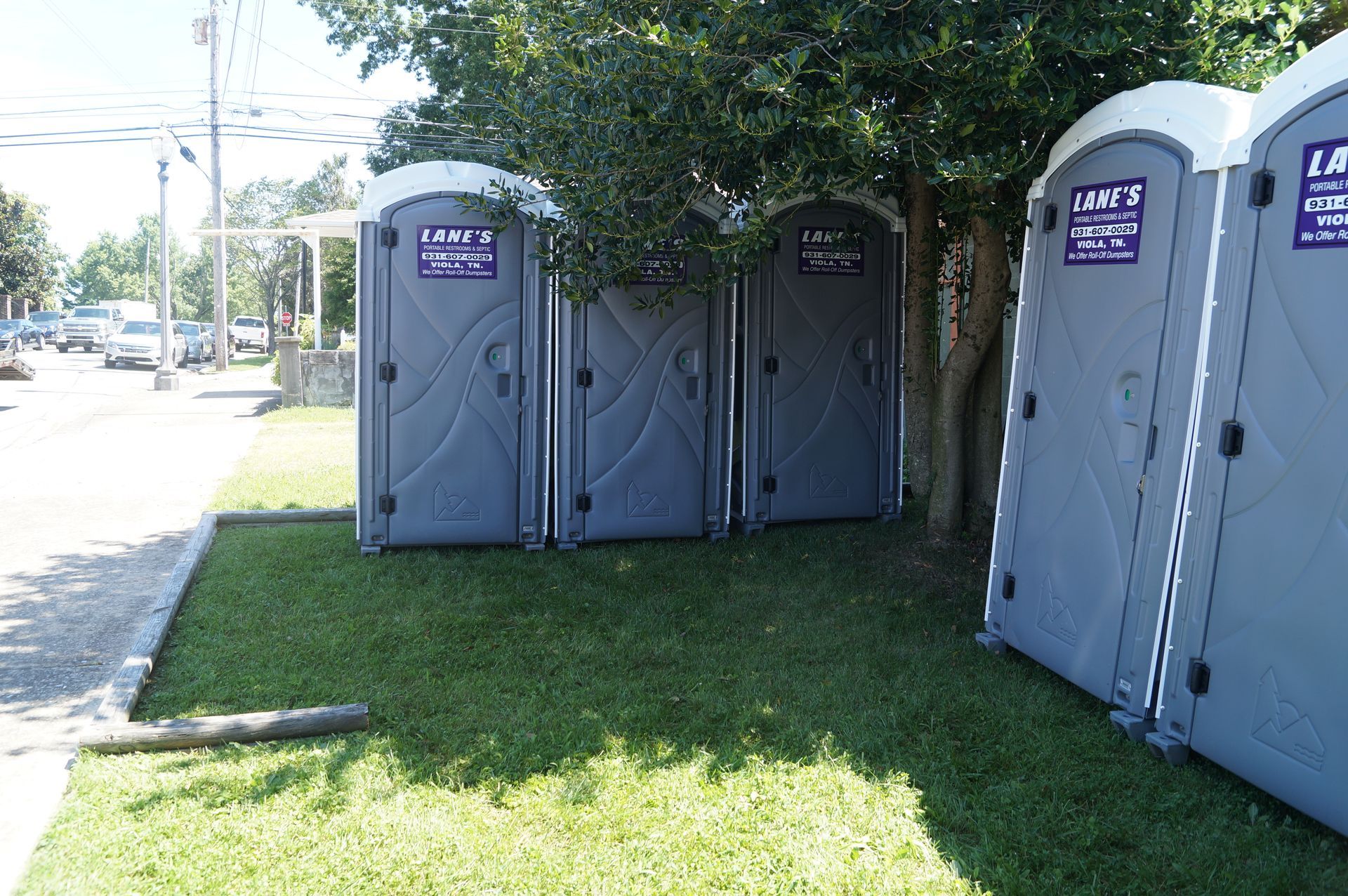 three portable toilets are lined up in a grassy area .