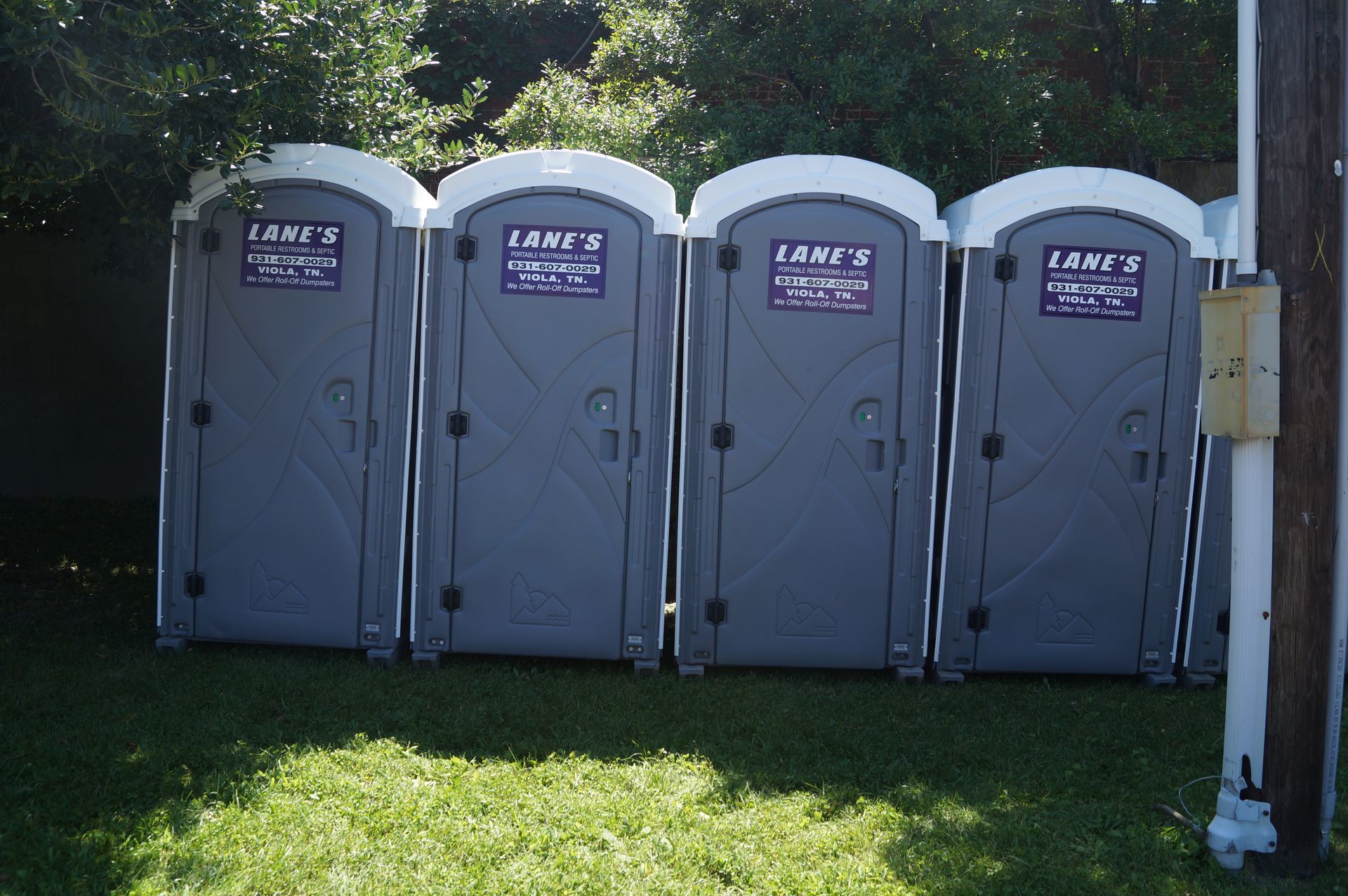 four lane 's portable toilets are lined up in a grassy yard