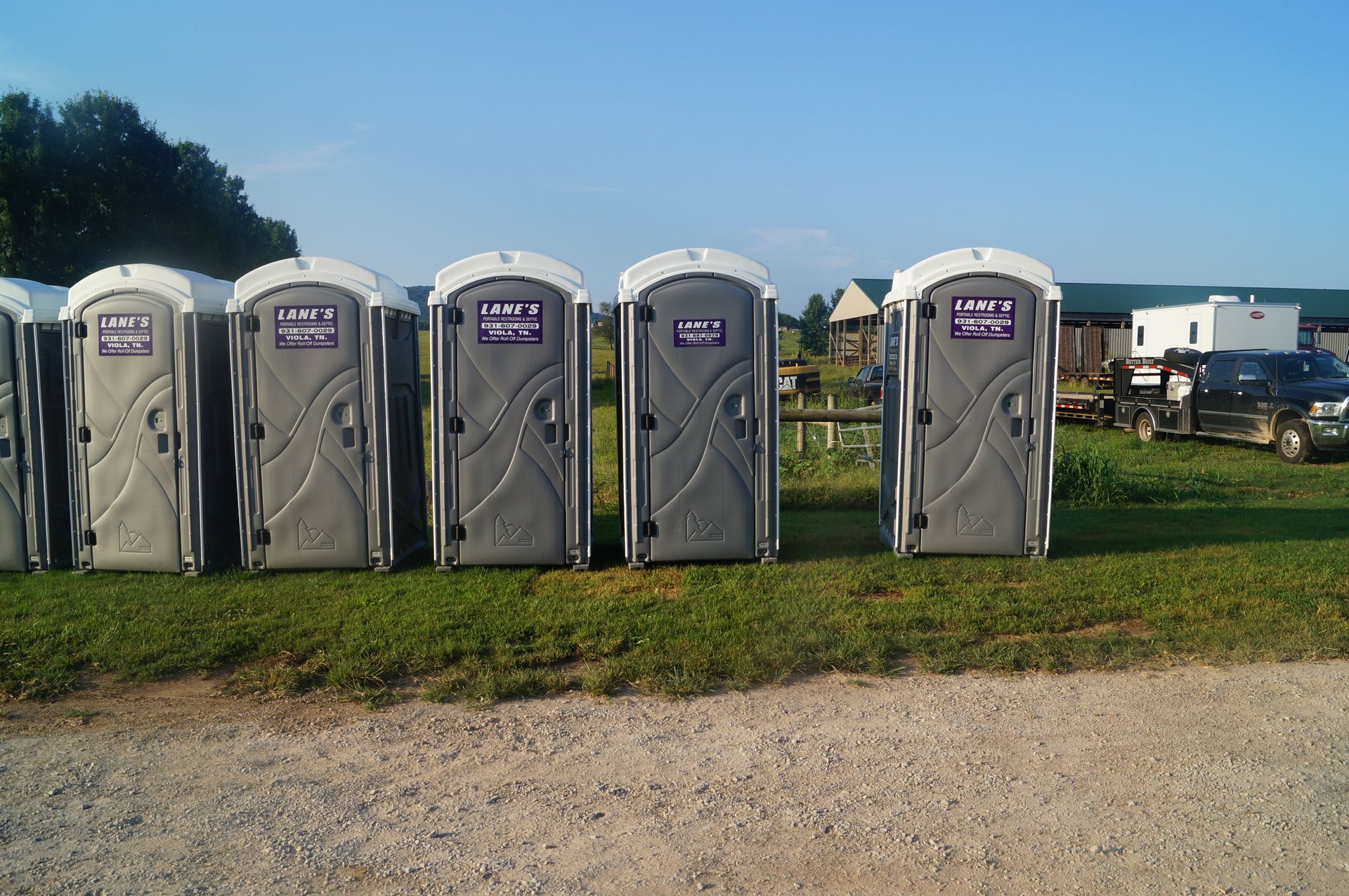 a row of portable toilets are lined up in a grassy field .