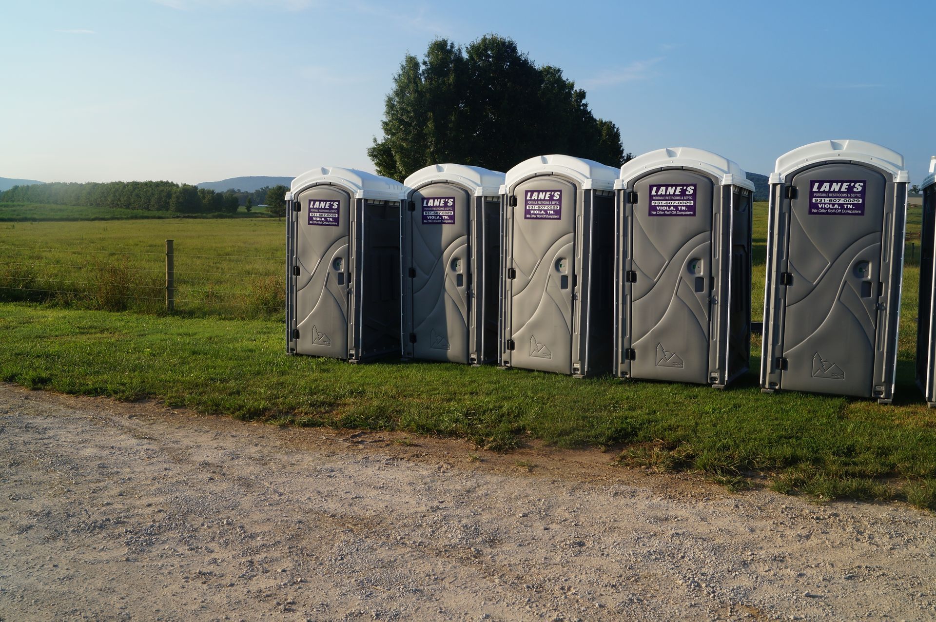 a row of portable toilets are lined up in a grassy field